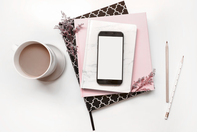 Coffee cup, smart phone, notebooks, pink desk flat lay. 