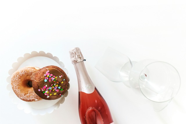 Donuts, blush sparkling wine, wine glasses flat lay