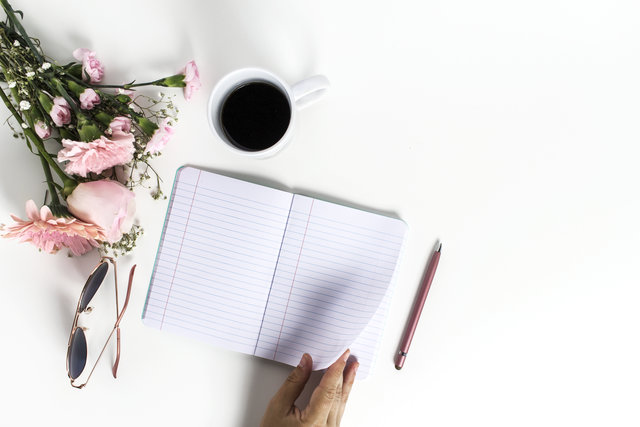 Pink flowers, sunglasses, coffee cup, notebook, pink pen flat lay