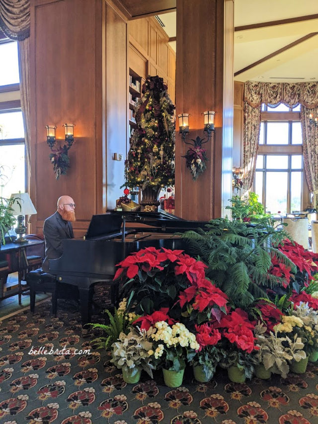 Man playing a grand piano, surrounded by Christmas decorations and fresh flowers