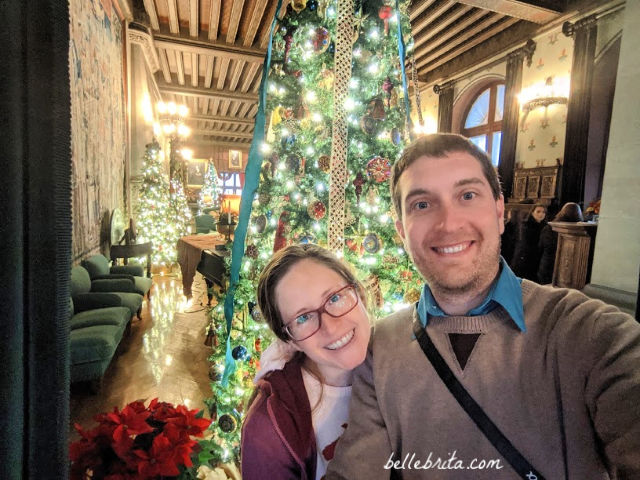 Woman and man smiling, standing in front of a row of Christmas trees at Biltmore