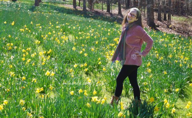 White woman wearing pink Marley Lily sweater and black Pact leggings standing in a field of daffodils.