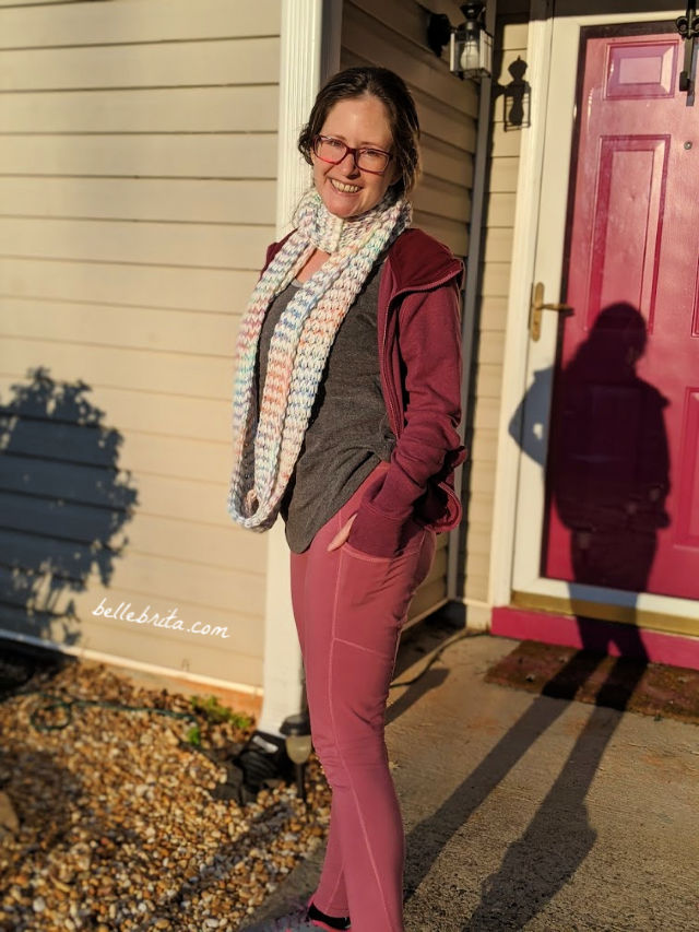 White woman wearing pink Pact leggings, standing in front of a pink door. 