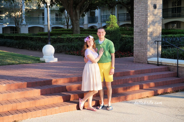 White woman in a pink and purple outfit with a white man in a green and yellow outfit. Disney Bounding Rapunzel and Pascal from Tangled.