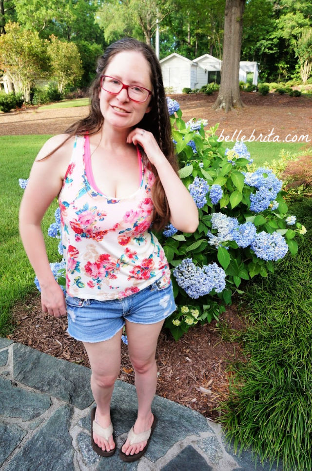 White woman wearing a floral tank top, standing in a garden