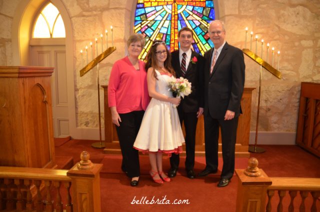 Wedding photo of white bride and groom, center. Mother of the bride is on the left. Father of the bride is on the right. 