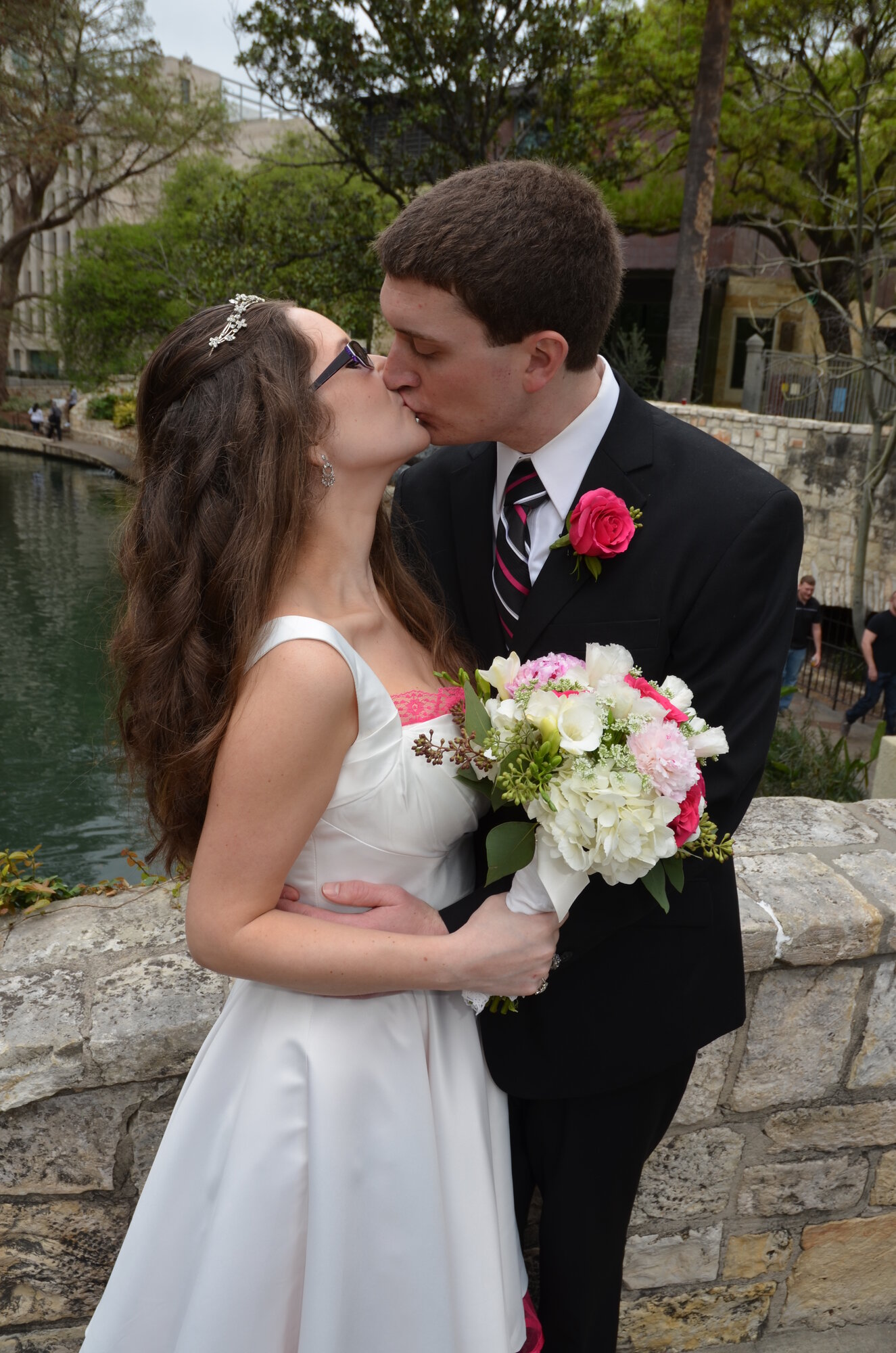 Brita and Dan on their wedding day, kissing while standing on a stone bridge in San Antonio.