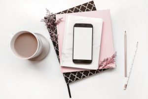 Coffee cup, smart phone, notebooks, pink desk flat lay.